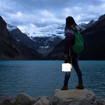 A woman holding a bright solar lantern while she's looking out over the sea